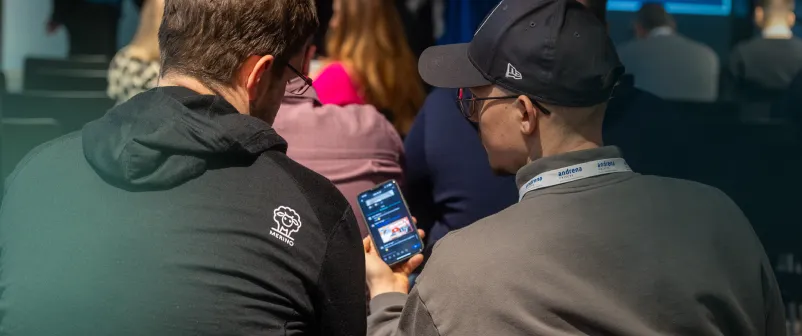 Zwei Teilnehmende einer früheren T4AT-Konferenz tauschen sich über ihre Smartphones aus